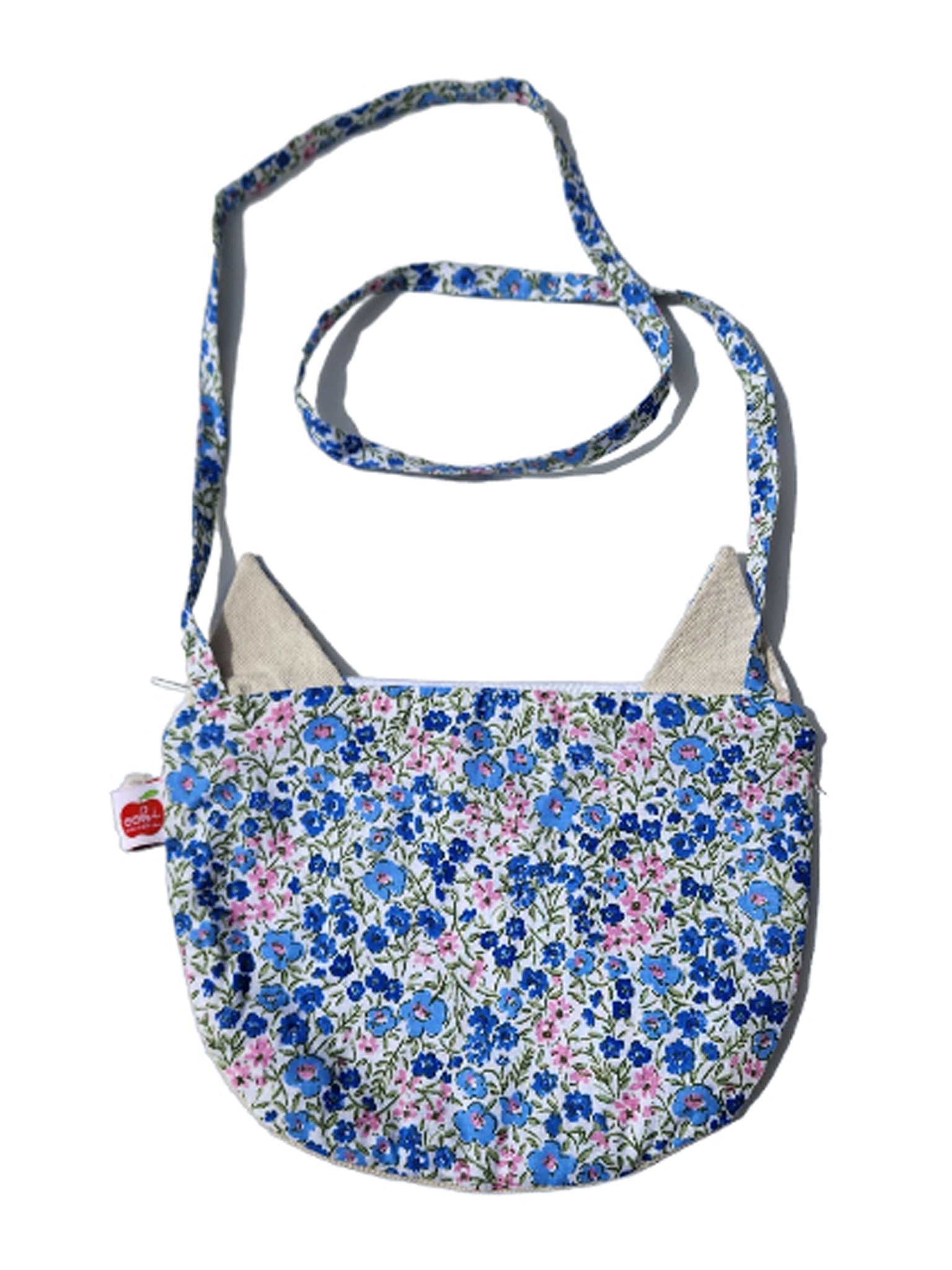 The Cat Bag by Oobi is a fabric bag adorned with blue, pink, and white floral patterns, featuring a long strap and cat ear-shaped accents.