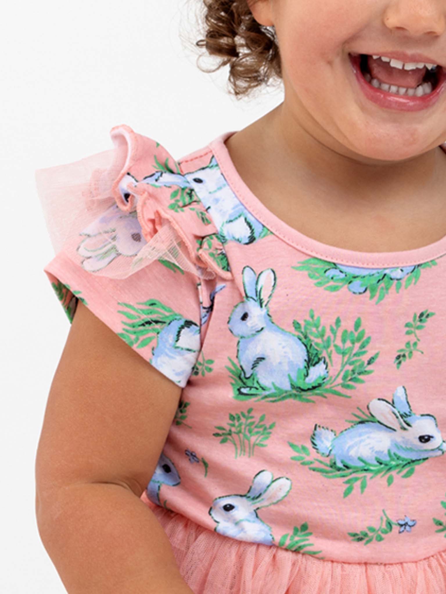 A child wearing the Pink Bunnies Ariel Dress by Bunny, featuring a white bunny print and ruffled sleeves, beams with a bright smile.