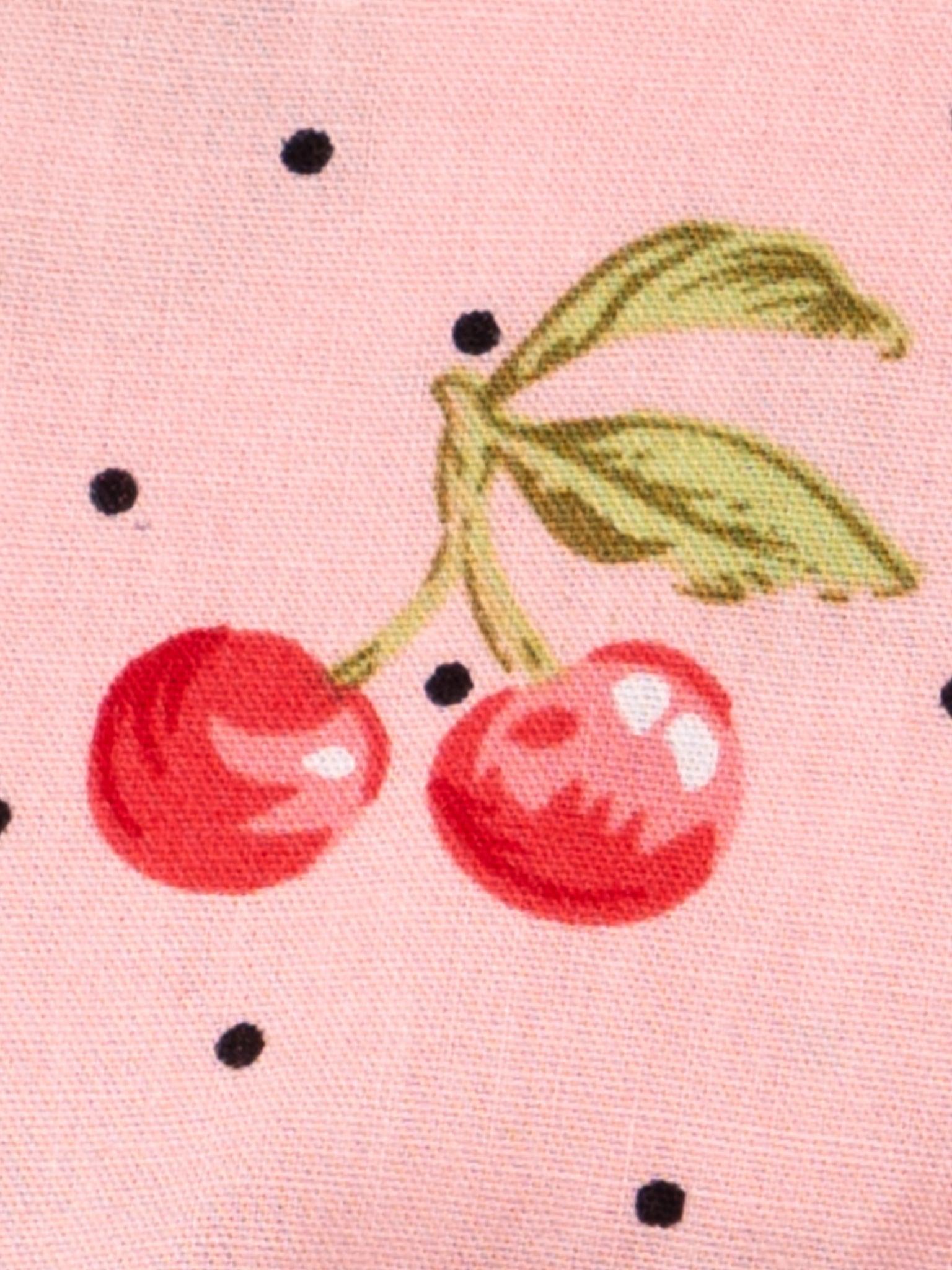 A close up of a pink fabric with cherries on it.