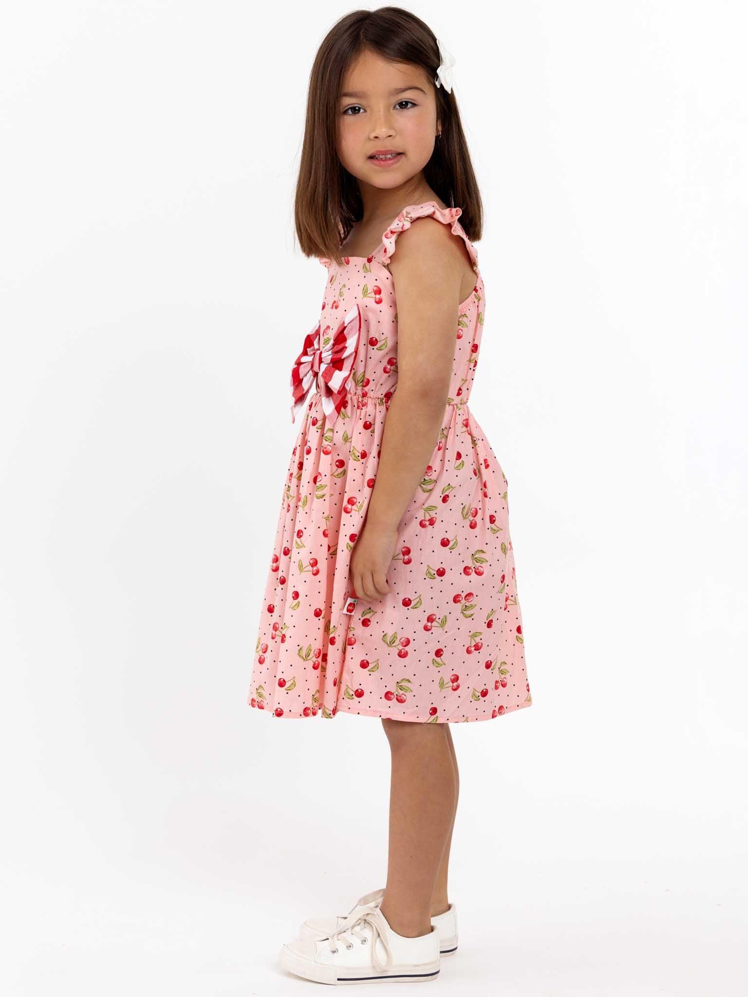 A little girl in a pink Mia dress standing in front of a white background.