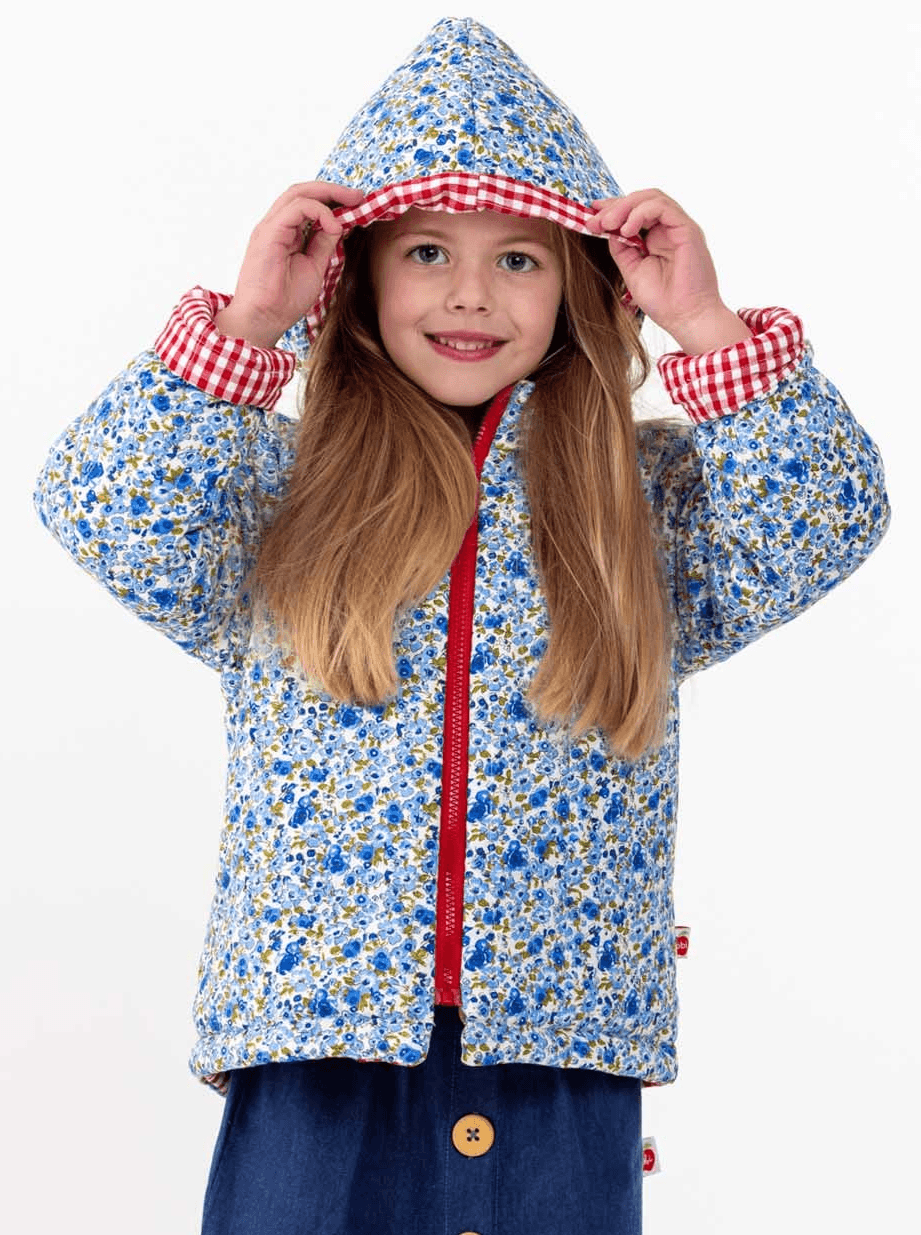 Young girl in English Wildflowers' English Flowers Hooded Reversible Jacket and red plaid hood smiling at the camera, isolated on white background.