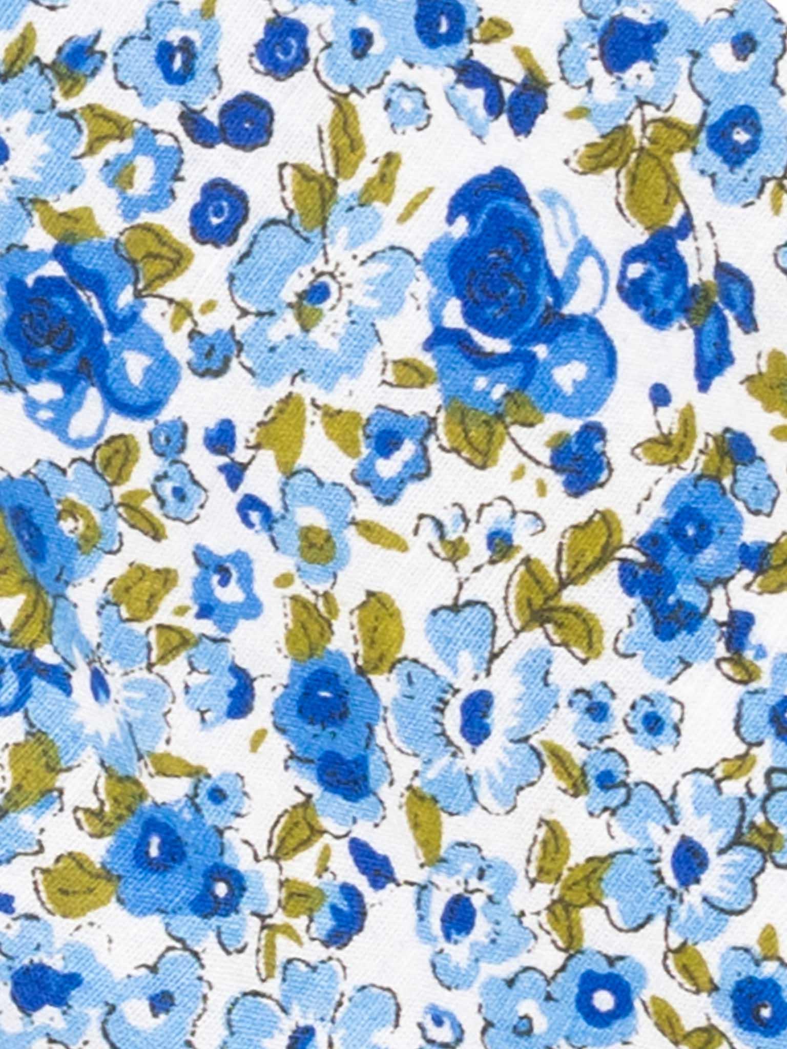 Close-up of a English Wildflowers floral quilted jacket fabric pattern featuring blue roses and smaller blue flowers with green leaves on a white background.