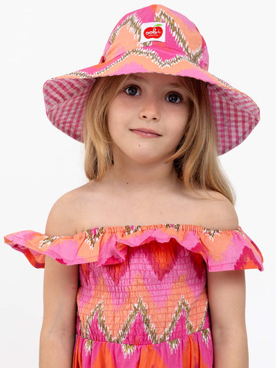 A young girl in a colorful Garden Party Dress and a Golden Ikat Bucket Hat stands in front of a plain background.