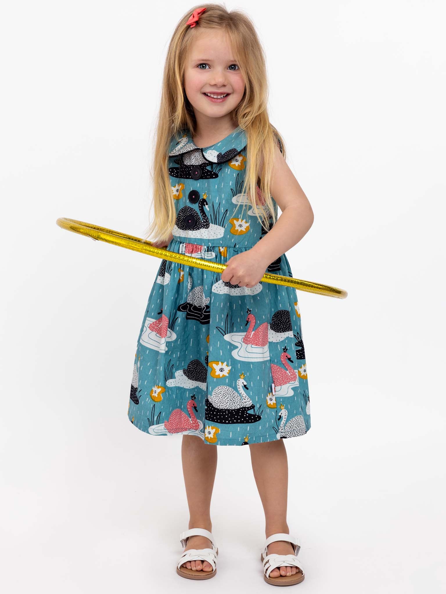 A young girl with long blonde hair in a Swan Song Gatsby Dress featuring animal prints holds a yellow hula hoop.