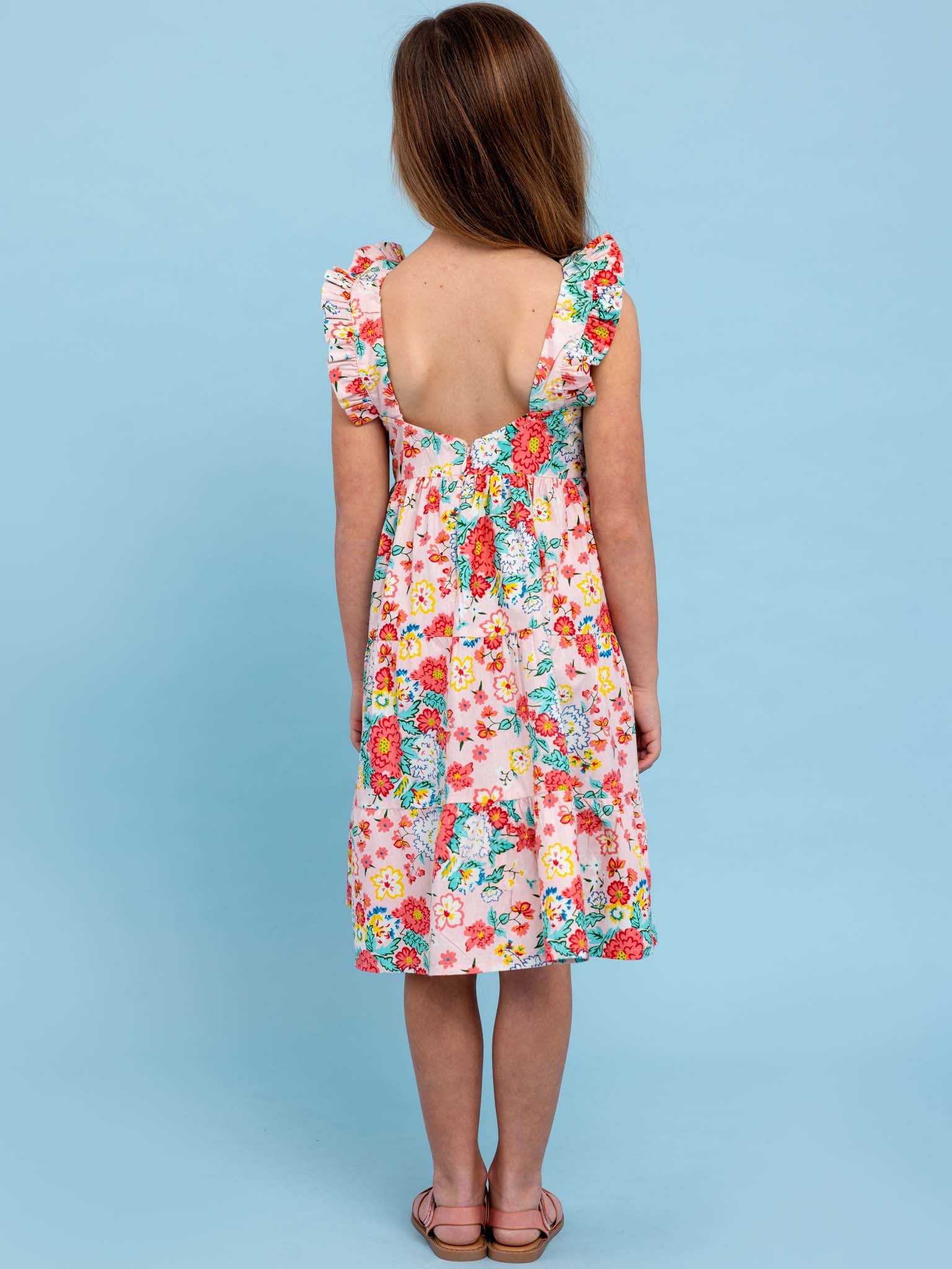 The back view of a girl in a Cornflower Wild Meadow Maxi Dress amidst flowers in bloom.