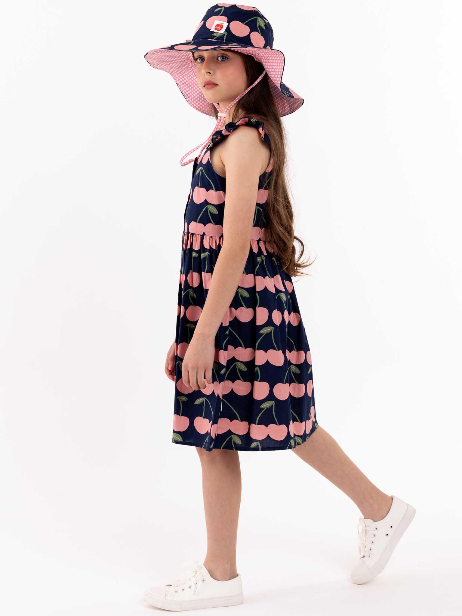 A little girl wearing a Navy Cherry Calista Dress and hat for summer.