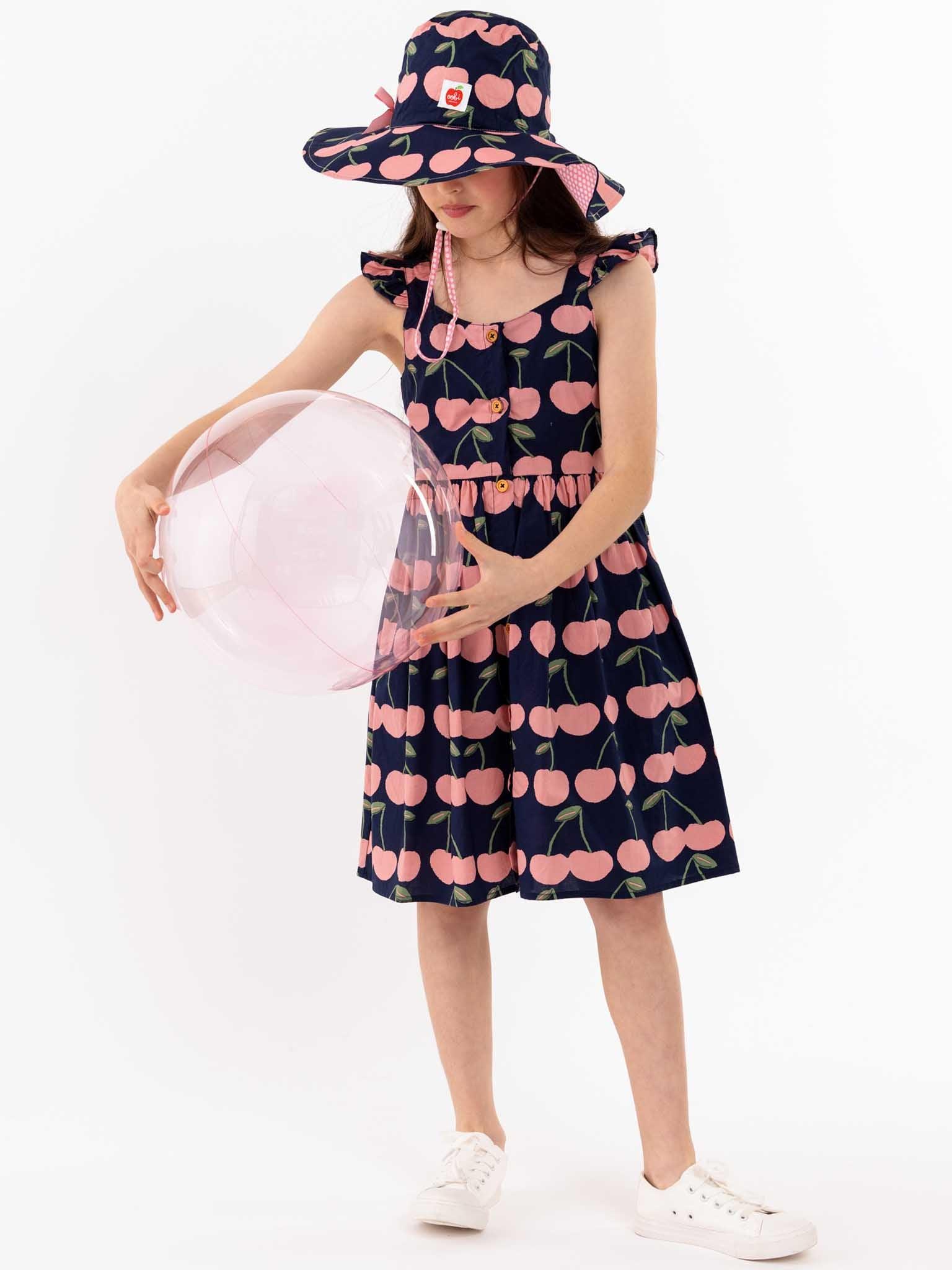 A girl wearing a Navy Cherry Calista Dress by Navy Cherry with cherries on it.