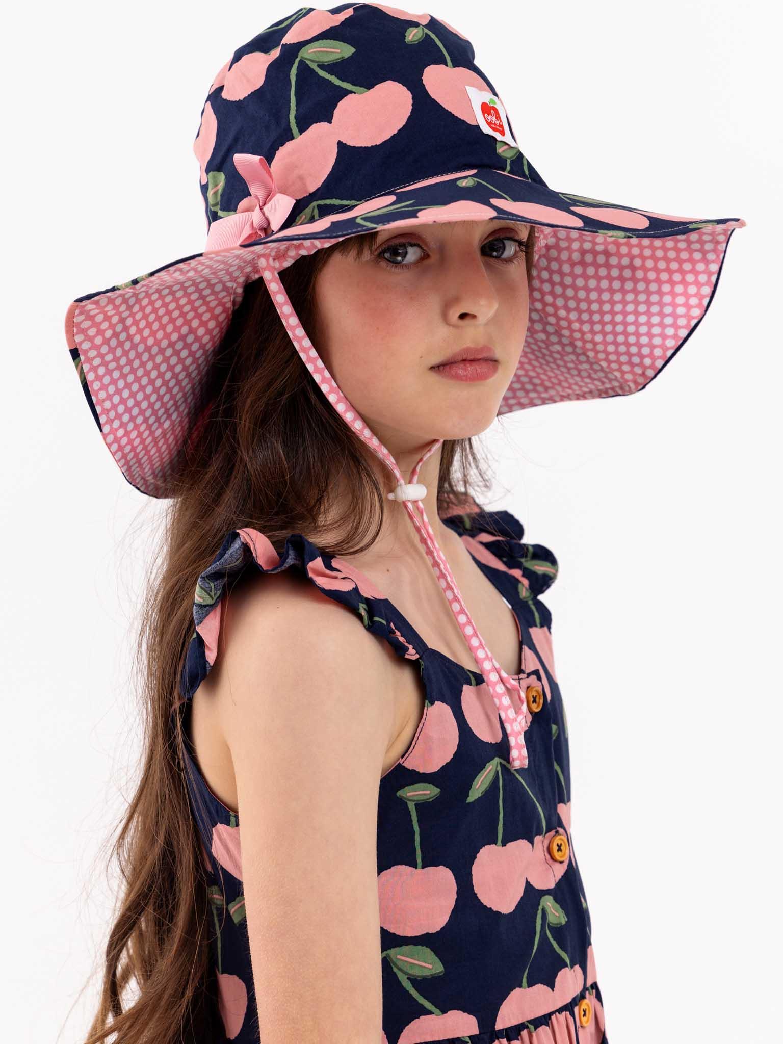 A young girl wearing a Navy Cherry Calista Dress with cherries on it in the summertime.