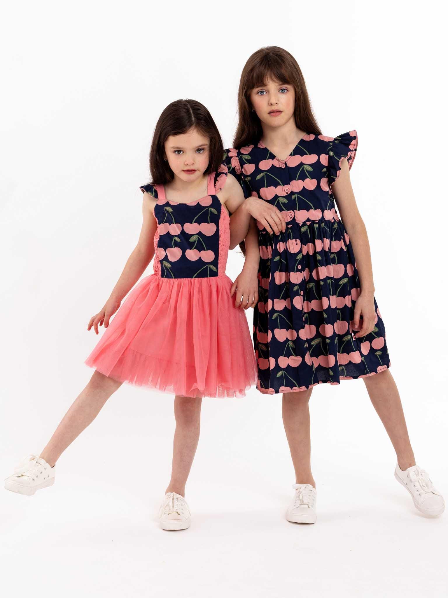 Two little girls in Navy Cherry Madison dresses posing for a photo.