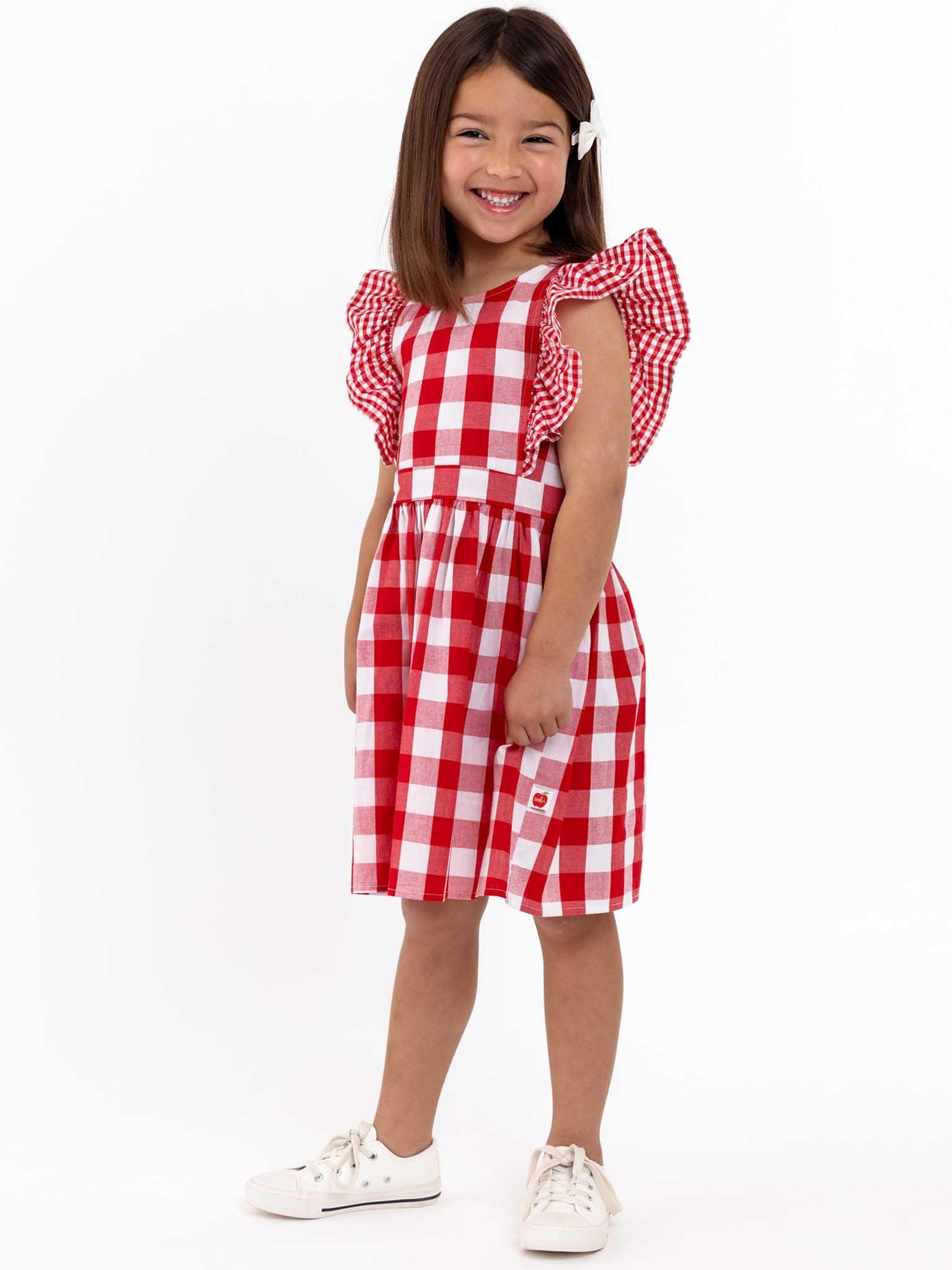 A little girl wearing an oversized ruffle sleeve Red Check Jayne dress with a gingham waistband.