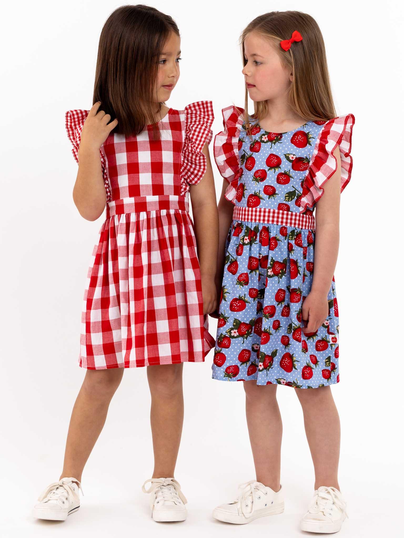 Two little girls are standing next to each other in a Red Check Jayne Dress by Red Check.