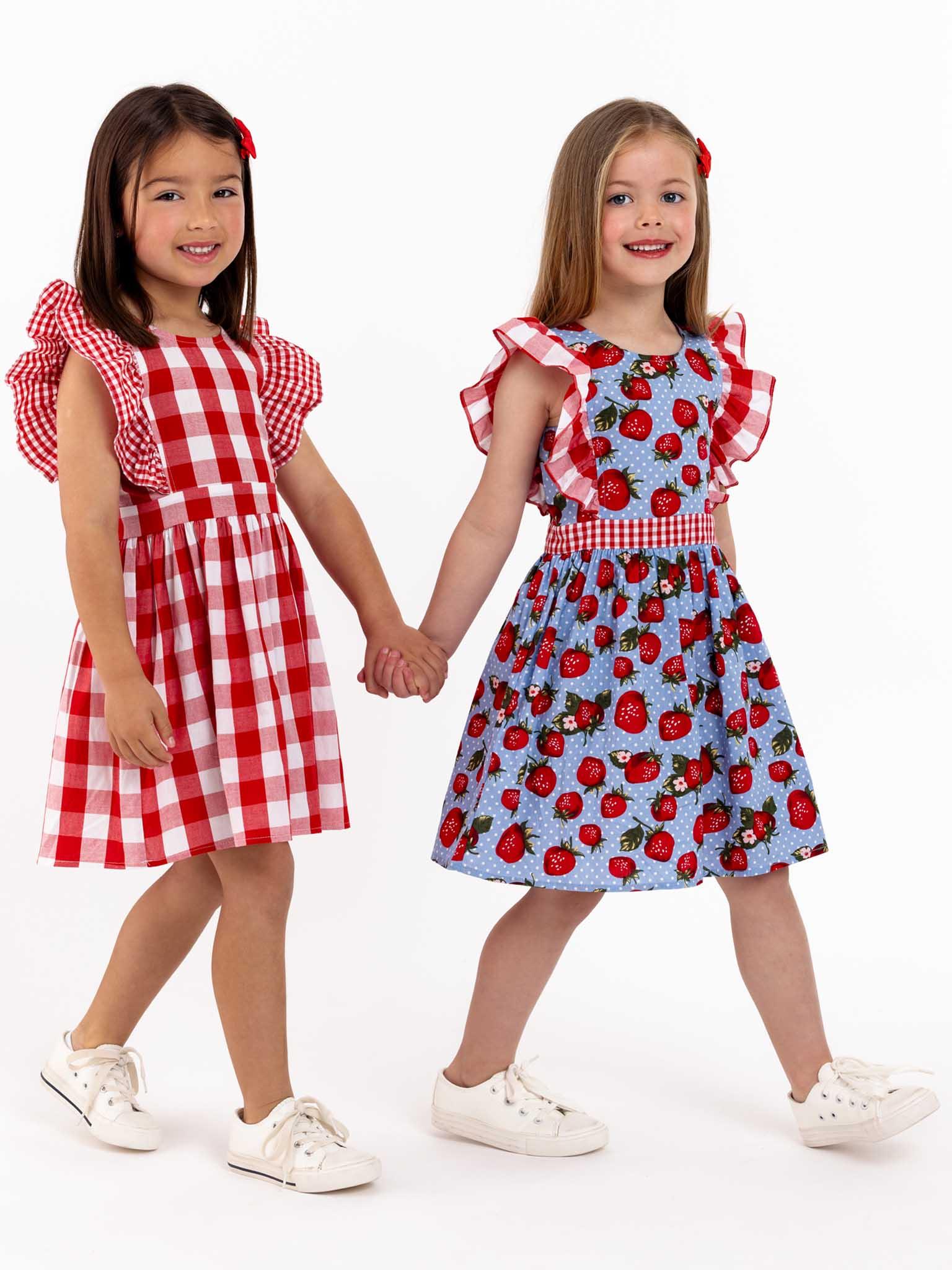 Two little girls are holding hands while wearing Red Check Jayne Dresses with oversized ruffle sleeves.