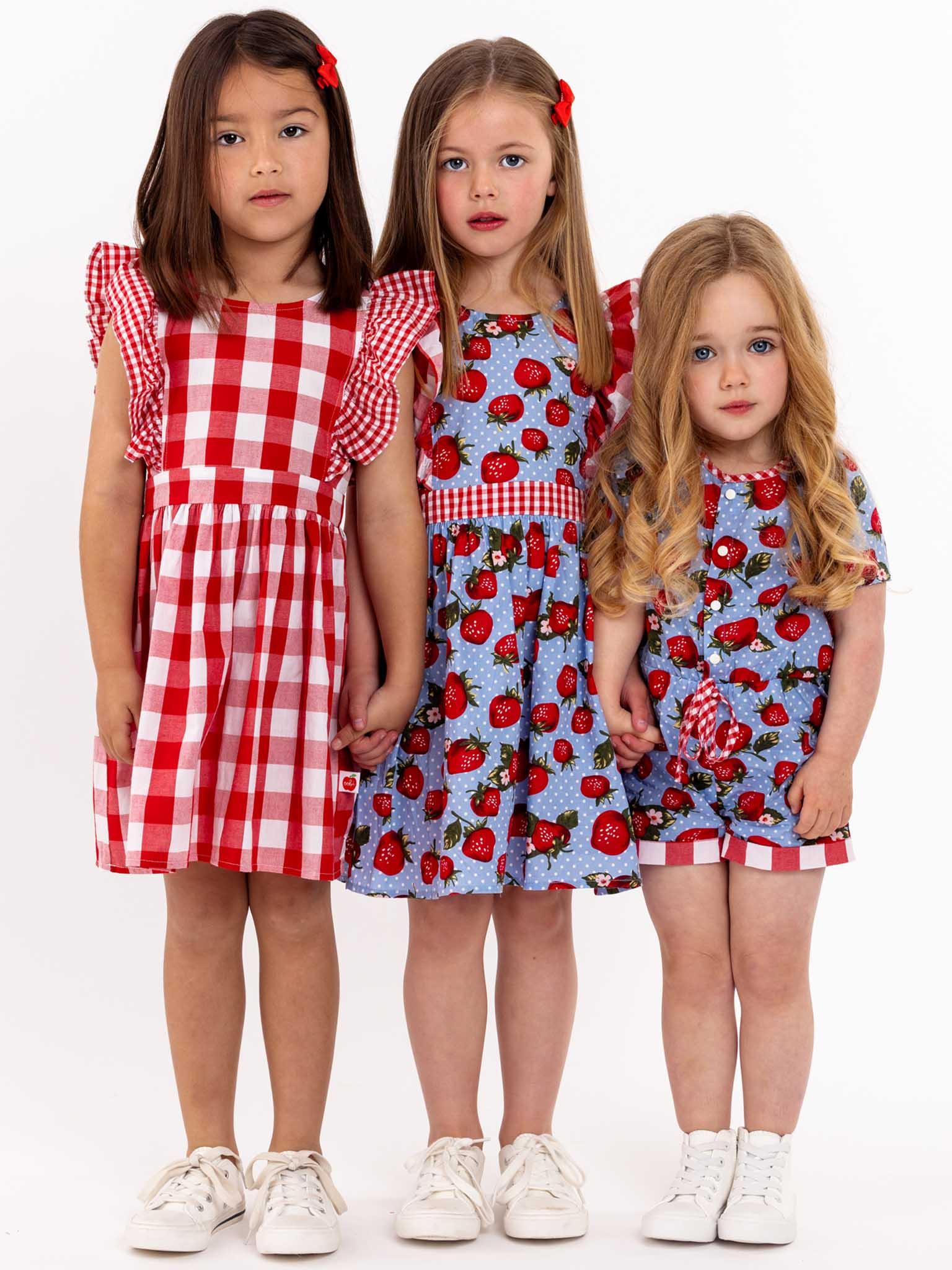 Three little girls wearing oversized ruffle sleeve Red Check Jayne dresses with a Red Check waistband.