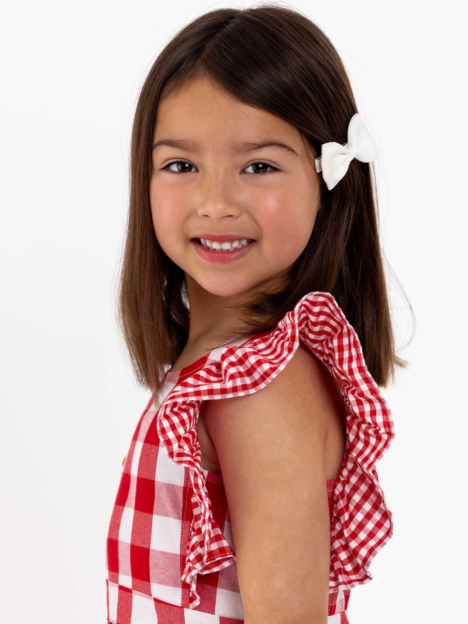 A little girl wearing an oversized ruffle sleeve Red Check Jayne dress with a gingham waistband.