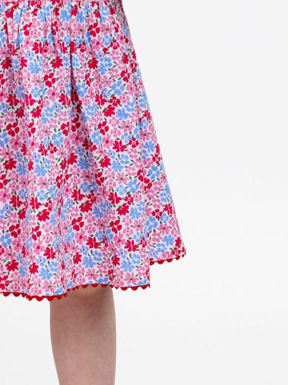 A close-up of the Cottage Flowers "Red Cottage Flowers Lace Edge Dress," showcasing its sweet red, blue, and pink flower pattern. The dress features a gathered waist, a lace-trimmed hem, and delicate ruffly sleeves.