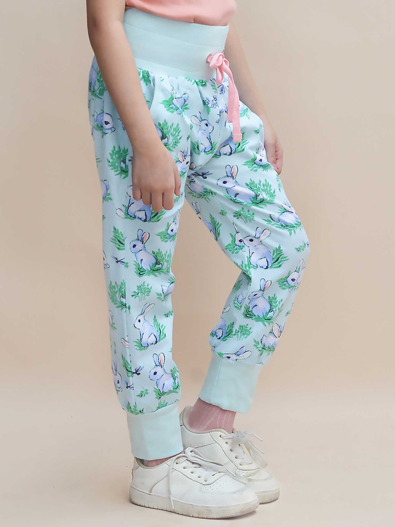 Against a neutral background, someone wears Bun-Buns' Blue Bun-Buns Soft Jersey Pants featuring a bunny print and pink waistband, paired with white sneakers. As a best seller, these pants stylishly complement the matching Zadie Jacket.