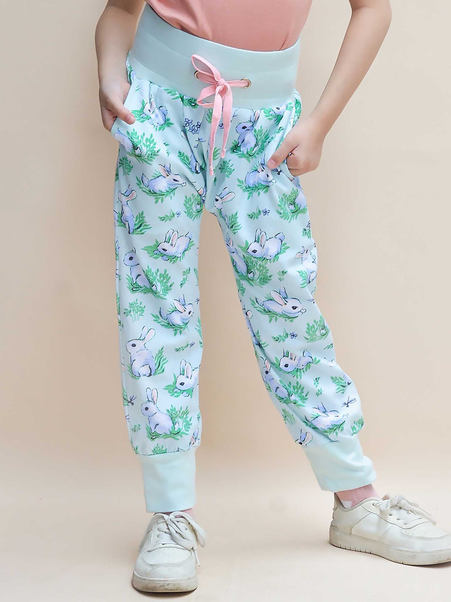 A child is in Blue Bun-Buns Soft Jersey Pants by Bun-Buns, featuring a bunny pattern, pink drawstring, and paired with white shoes and hands in pockets. These pants are ideal for complementing the matching Zadie Jacket to complete the look.