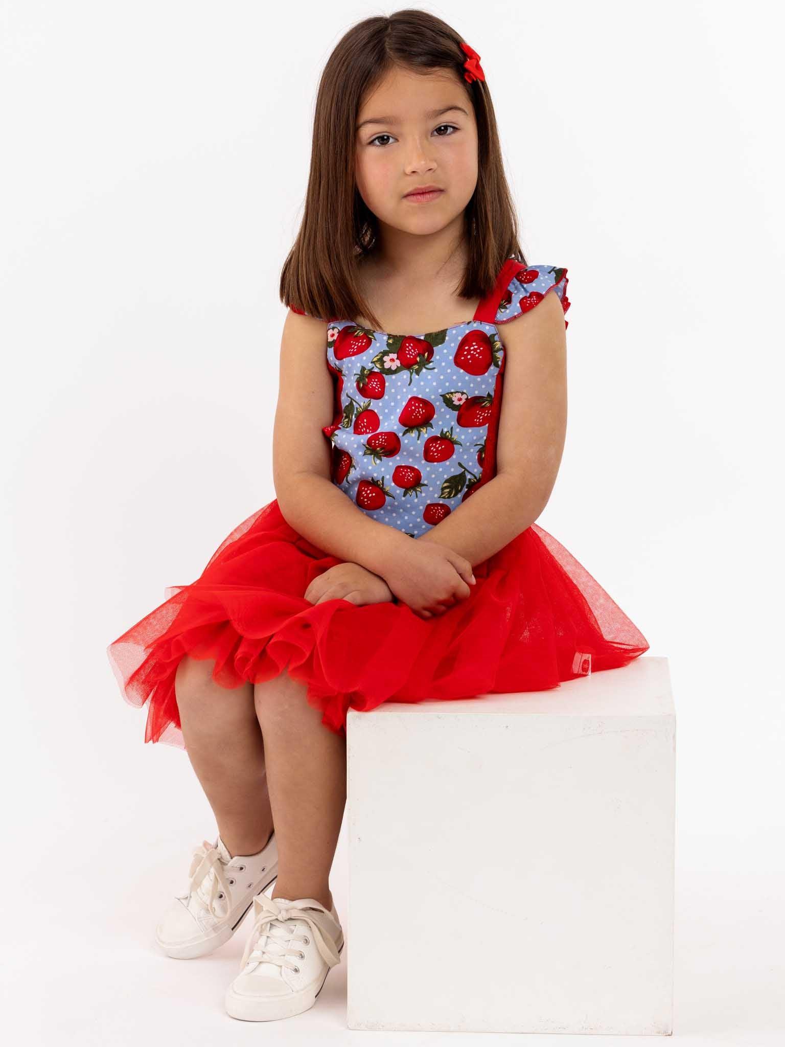 A little girl twirling in a Strawberry Fields Belle Tutu Dress on a white box.