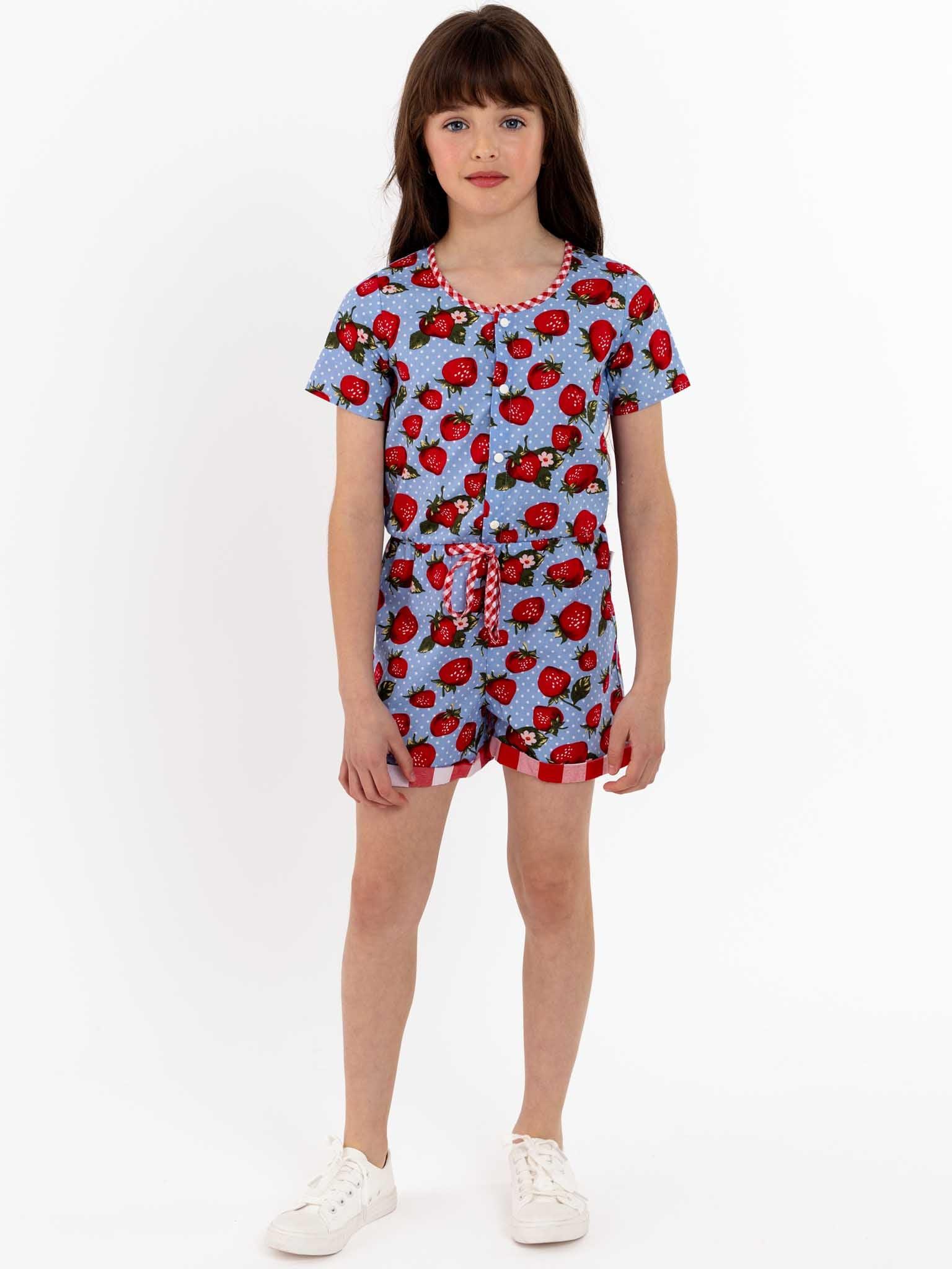 An easy-to-wear Strawberry Fields Maisy Playsuit for a young girl in a blue and red strawberry print, with press studs.