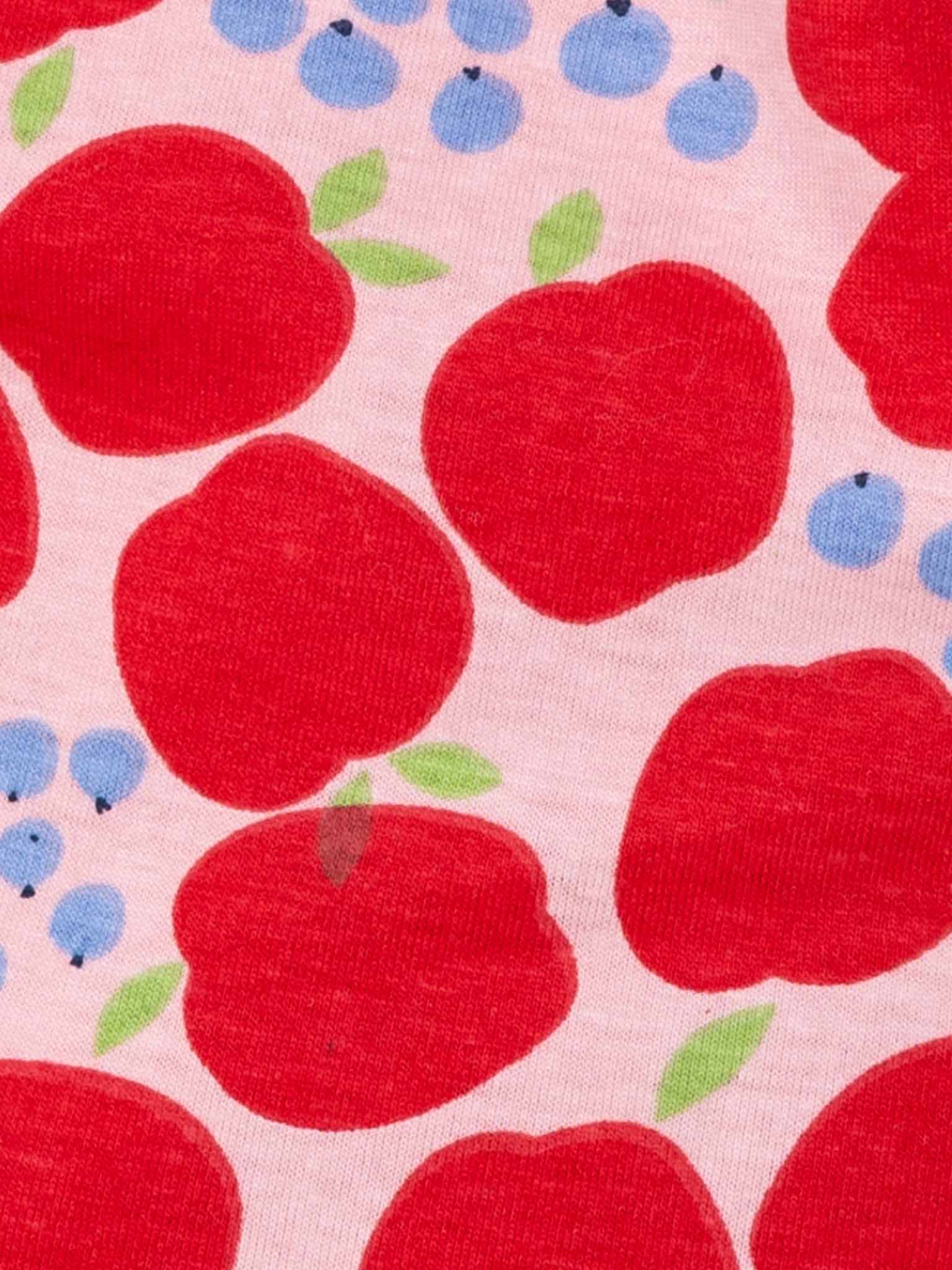 A Sweet Apple Amelie Dress showcasing a delightful print of large red apples with green leaves and small blue berries on a light pink background.