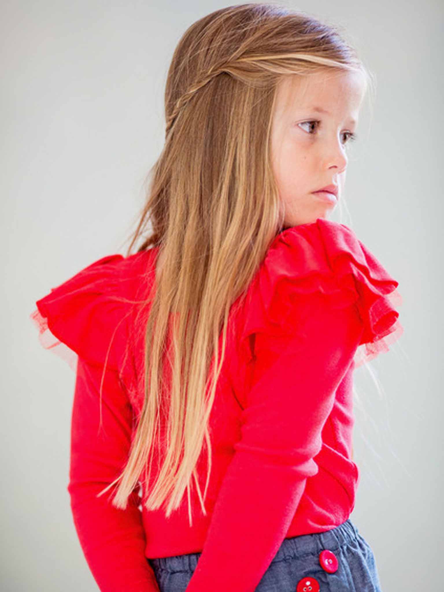 A young girl with long blonde hair, wearing the Essentials Sweetheart Red Tee - L/S with net 'flutter' sleeves, gazes to the side.