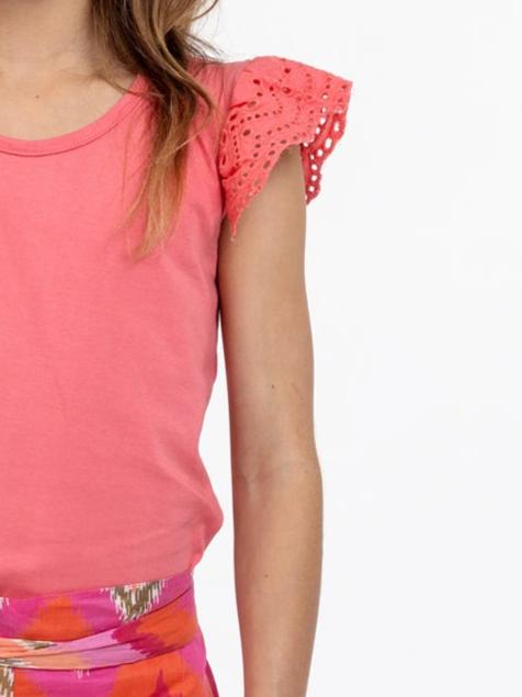 Child wearing an Essentials Lace Sleeve Primrose Pink Tee, paired with a colorful patterned skirt. Shoulders up image with a focus on the intricate clothing details.