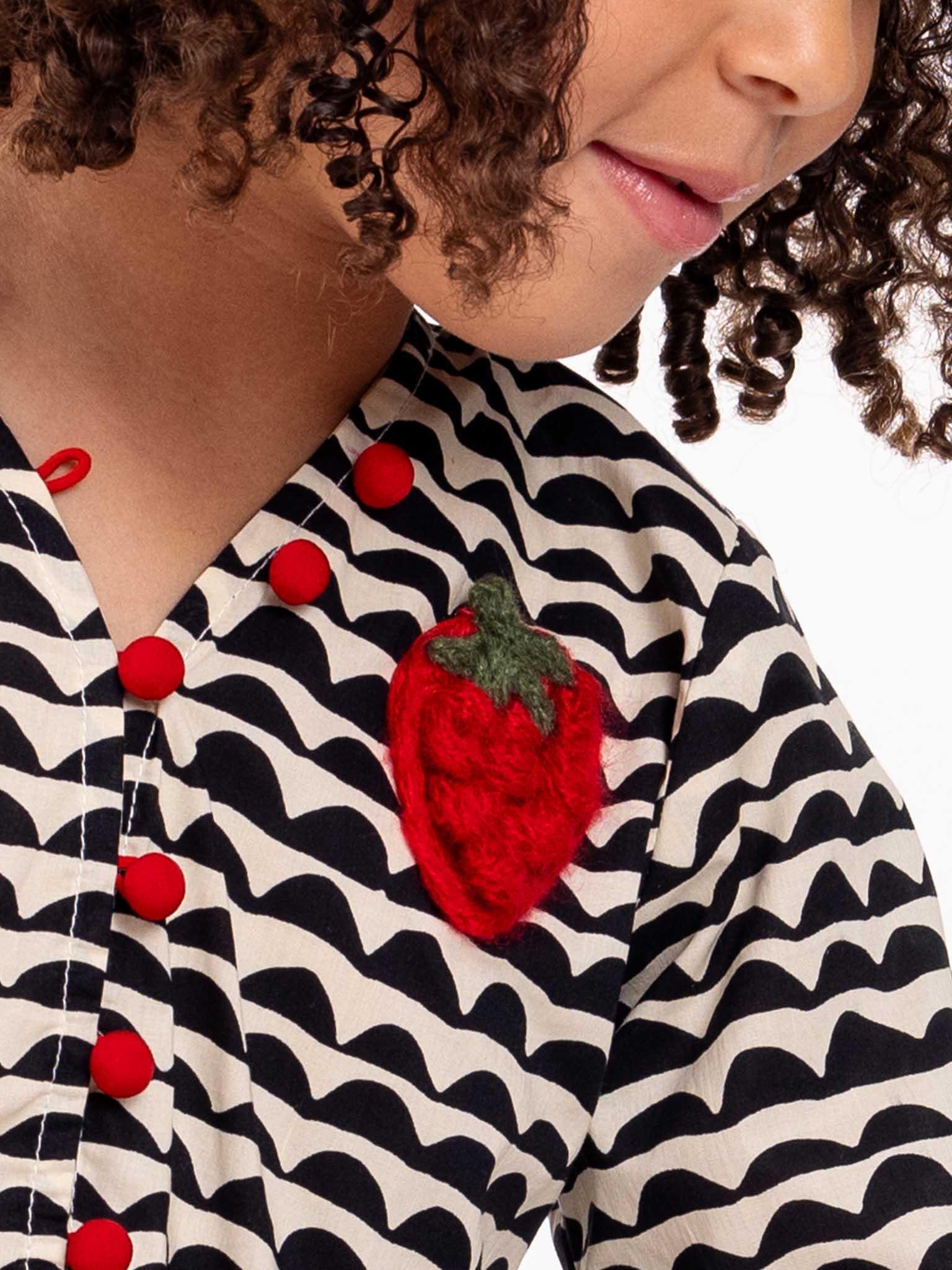 Close-up of a woman's torso wearing a zebra print Wiggly Adriana dress with red buttons, decorated with a textured strawberry brooch.