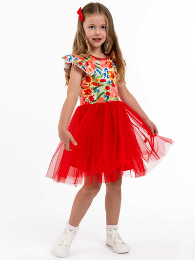 A young girl wearing the exquisite Wild Roses Ariel Dress, featuring a vibrant floral print, stands against a plain background. Her outfit is completed with a red tulle skirt and white shoes, making her perfectly dressed for any party occasion.