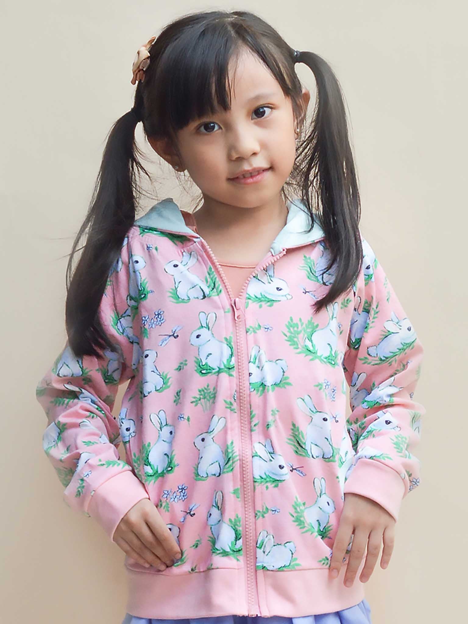 A young girl confidently models the Bun-Buns Pink Bun-Buns Zadie Jacket, featuring charming bunny prints, against a plain background.